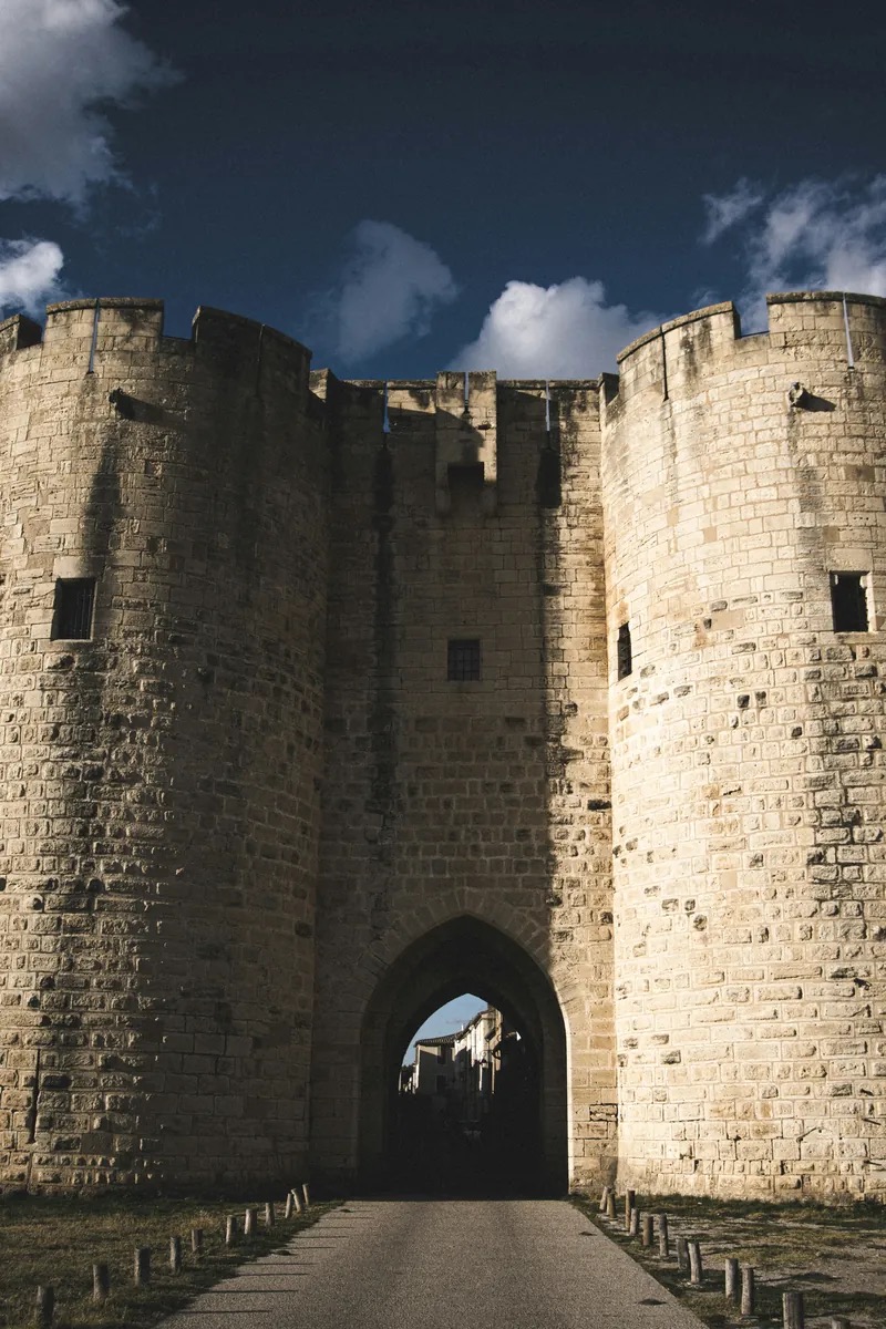 Die mittelalterlichen Stadtmauern und der mächtige, zylindrische Tour de Constance von Aigues-Mortes erheben sich über der flachen Camargue, ihr heller Stein leuchtet in der goldenen Stunde, dahinter die Salzwasserseen. Aigues-Mortes, Okzitanien, Frankreich.